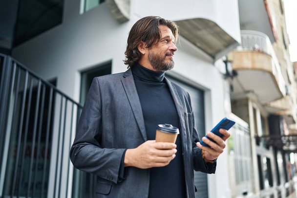 Middelbare leeftijd man met smartphone het drinken van koffie op straat - Foto, afbeelding