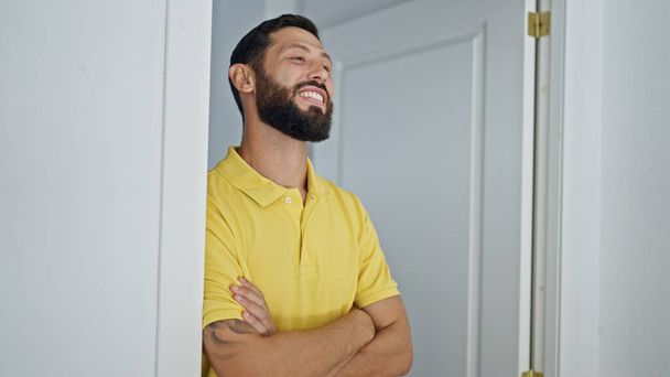 Young hispanic man leaning on door with arms crossed gesture at home - Photo, Image