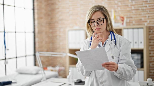 Young blonde woman doctor reading document at clinic - Photo, Image
