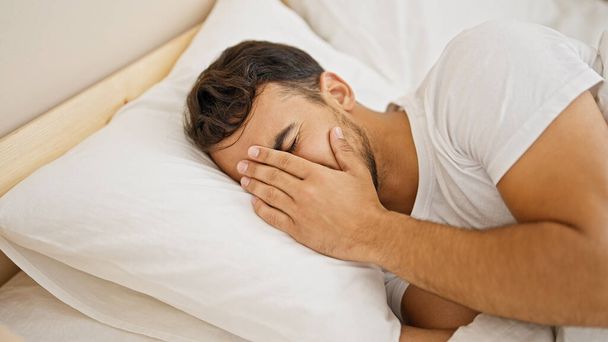 Молодой латиноамериканец лежит на кровати и плачет в спальне - Фото, изображение