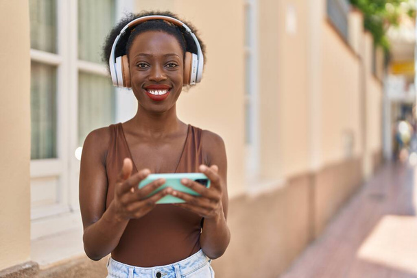 Mujer afroamericana sonriendo confiada viendo video en smartphone en la calle - Foto, imagen