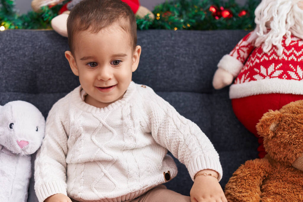 Adorabile bambino ispanico sorridente fiducioso seduto sul divano dalla decorazione natalizia a casa - Foto, immagini