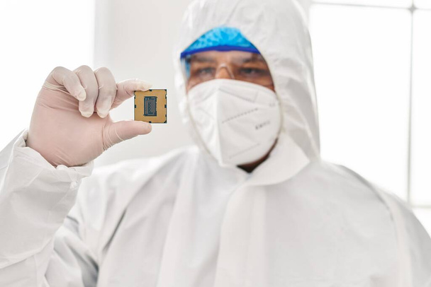 Junger lateinamerikanischer Wissenschaftler in Schutzuniform hält CPU-Prozessor-Chip im Labor - Foto, Bild