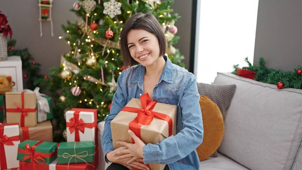 Elinde Noel hediyesi olan beyaz bir kadın evdeki kanepede oturuyor. - Fotoğraf, Görsel