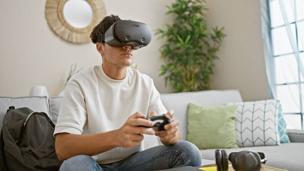 Engrossi jeune adolescent hispanique plonge dans l'univers du jeu à la maison, en utilisant des lunettes de réalité virtuelle et joystick, vivant un mode de vie 3D détendu mais concentré - Photo, image