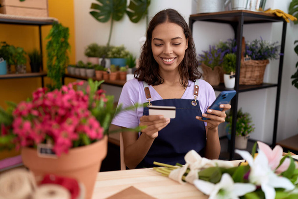 Joven florista afroamericana mujer usando teléfono inteligente con tarjeta de crédito en la tienda de flores - Foto, imagen