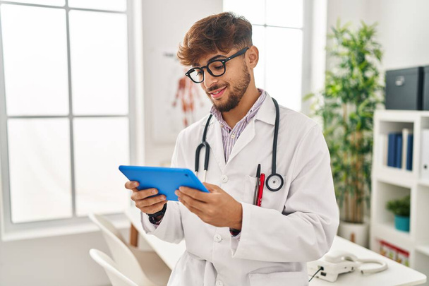 Young arab man wearing doctor uniform using touchpad working at clinic - Foto, afbeelding