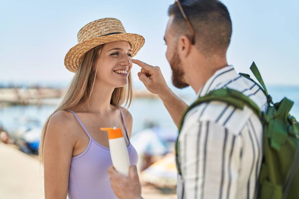 Мужчина и женщина туристы улыбаются уверенно нанося солнцезащитный крем на лицо на море - Фото, изображение