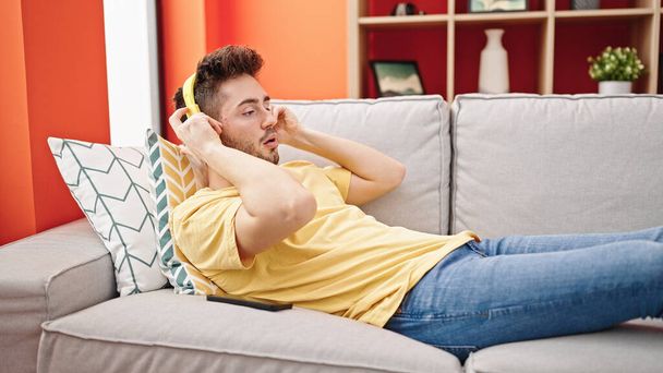 Genç İspanyol adam evdeki kanepede uzanmış müzik dinliyor. - Fotoğraf, Görsel