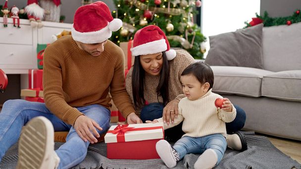 Paar und Sohn beim Auspacken von Geschenk zu Hause am Weihnachtsbaum sitzend - Foto, Bild