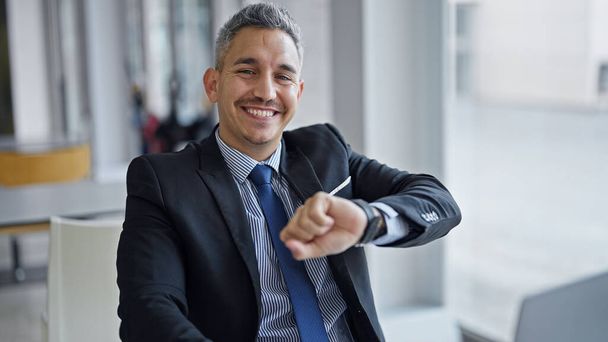 Молодой латиноамериканец бизнесмен улыбается уверенно глядя на часы в офисе - Фото, изображение