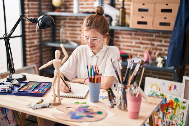 Giovane donna bionda disegno piccolo manichino su notebook in studio d'arte - Foto, immagini