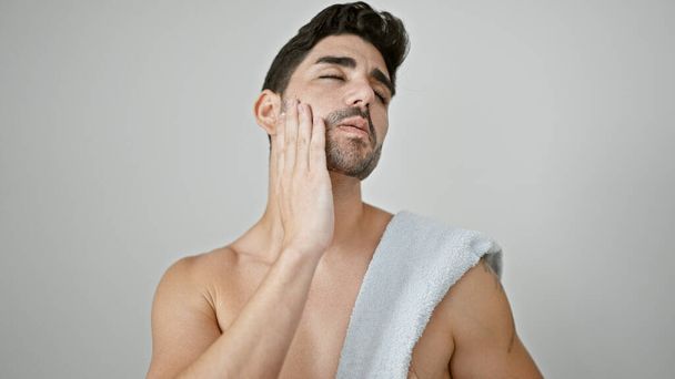 Genç İspanyol adam üstsüz duruyor ve beyaz arka planda sakal tedavisi uyguluyor. - Fotoğraf, Görsel