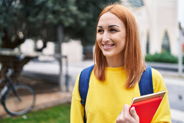 Young caucasian woman student smiling confident holding books at park - 写真・画像