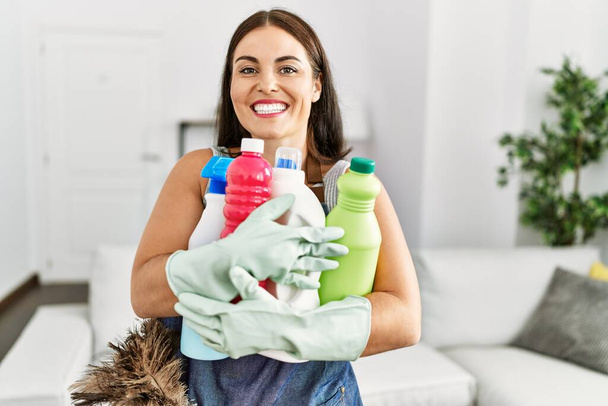 Jovem bela mulher hispânica sorrindo confiante segurando produtos limpos em casa - Foto, Imagem