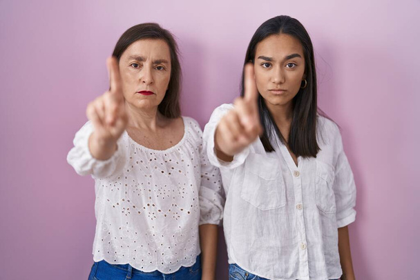 Hispanische Mutter und Tochter zeigen mit erhobenem Zeigefinger und wütendem Gesichtsausdruck zusammen und zeigen keine Geste  - Foto, Bild
