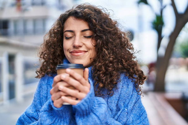 Молодая латиноамериканка с уверенной улыбкой пьет кофе на улице - Фото, изображение