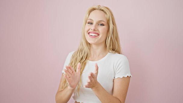 Nuori blondi nainen hymyilee luottavainen taputtaa kädet yli eristetty vaaleanpunainen tausta - Valokuva, kuva