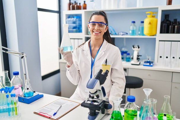 Spanyol nő dolgozik tudós laboratóriumban pozitív és boldog álló és mosolygó magabiztos mosollyal mutatja fogak  - Fotó, kép