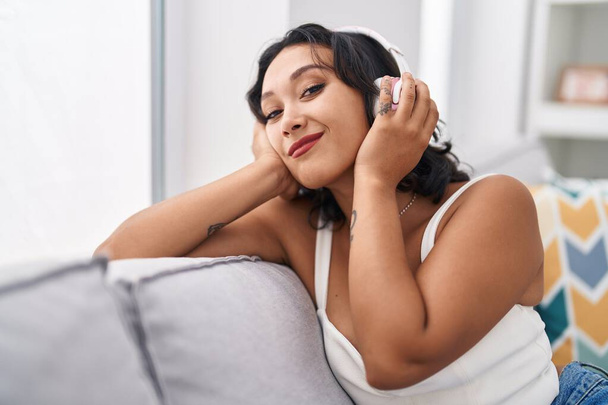 Nuori kaunis latino nainen kuuntelee musiikkia istuu sohvalla kotona - Valokuva, kuva