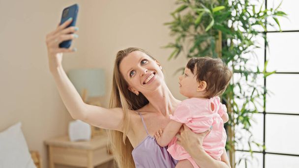 Mother and daughter sitting on bed make selfie by smartphone at bedroom - 写真・画像