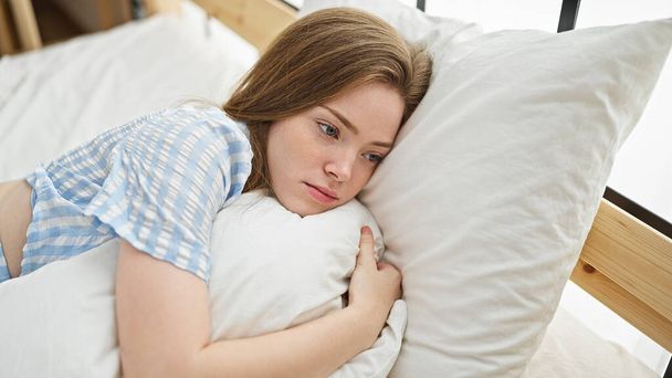 Jeune femme blonde allongée sur le lit avec un visage sérieux dans la chambre - Photo, image
