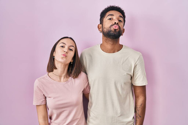 Junges hispanisches Paar zusammen auf rosa Hintergrund blickend in die Kamera, die einen Kuss in die Luft pustet, ist schön und sexy. Liebesausdruck.  - Foto, Bild