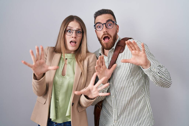 Young couple standing over white background afraid and terrified with fear expression stop gesture with hands, shouting in shock. panic concept.  - Photo, Image