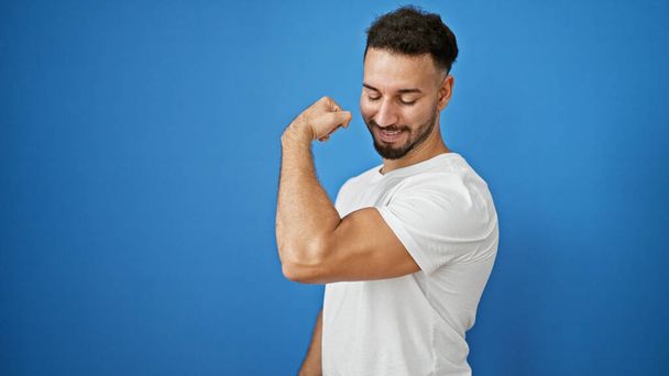 Young arab man smiling confident doing strong gesture with arm over isolated blue background - Foto, imagen