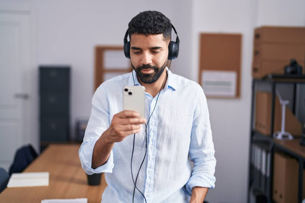 Young arab man business worker listening to music at office - 写真・画像