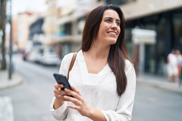Młoda piękna Latynoska uśmiecha się pewnie za pomocą smartfona na ulicy - Zdjęcie, obraz