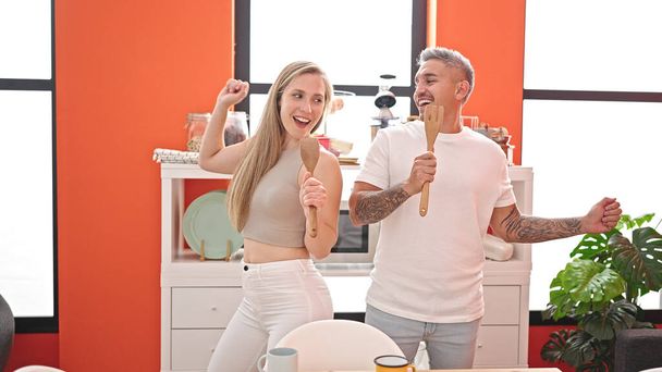 Mann und Frau singen und tanzen mit Küchenutensilien als Mikrofon im Esszimmer - Foto, Bild