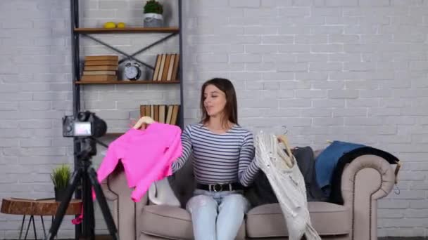 Atrakcyjna kobieta vlogger siedzi na kanapie, patrząc w kamerę i przemawiając przed kamerą na jej vlog pokazując ubrania. Prawdziwy film. Koncepcja Vlogging - Materiał filmowy, wideo
