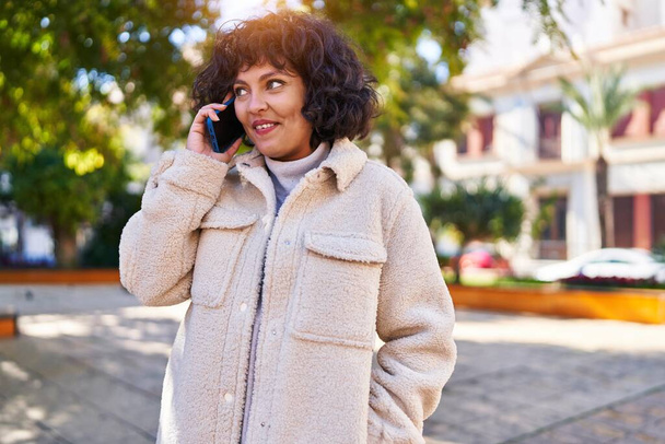 Junge schöne hispanische Frau lächelt selbstbewusst und spricht im Park mit dem Smartphone - Foto, Bild