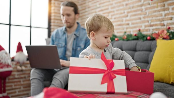 Padre e hijo desempaquetando el regalo de Navidad usando el ordenador portátil en casa - Foto, Imagen