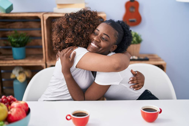 Mujeres afroamericanas madre e hija abrazándose bebiendo café en casa - Foto, imagen