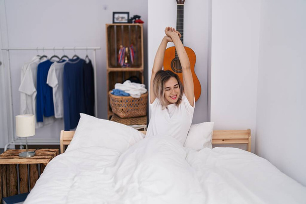 Young woman waking up stretching arms at bedroom - Fotoğraf, Görsel