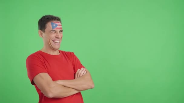 Video en estudio con croma de un hombre feliz con bandera puertorriqueña pintado en la cara mirando hacia el espacio de copia en blanco - Imágenes, Vídeo