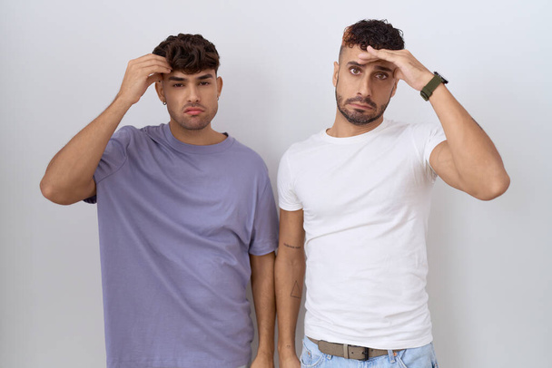 Homosexuální homosexuální homosexuální pár stojící nad bílým pozadím ustaraný a vystresovaný z problému s rukou na čele, nervózní a nervózní z krize  - Fotografie, Obrázek