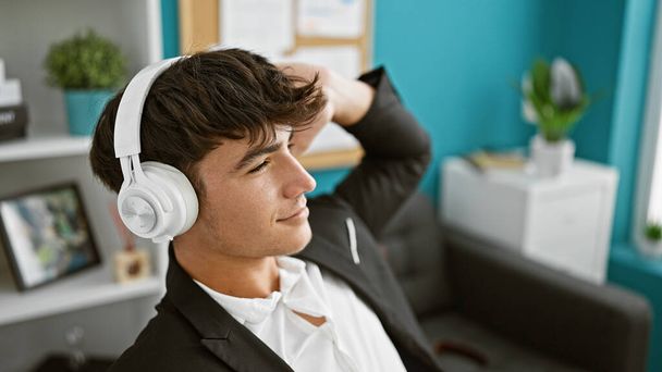 Glimlachende, stijlvolle jonge Spaanse tiener zakelijke werknemer vibing naar muziek tijdens het werken in een levendige kantooromgeving - Foto, afbeelding
