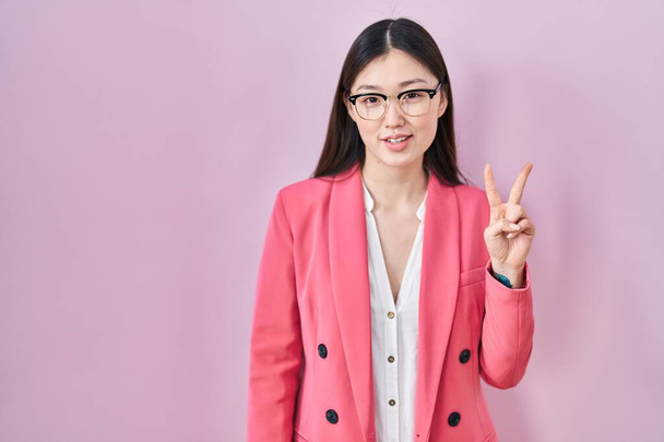 Čínský obchod mladá žena nosí brýle ukazující a ukazující nahoru s prsty číslo dvě při úsměvu sebevědomě a šťastně.  - Fotografie, Obrázek