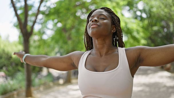 Afroamerikanerin lächelt selbstbewusst und atmet mit offenen Armen im Park - Foto, Bild