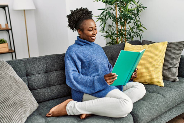 Африканська американка читає книжку, сидячи на дивані вдома. - Фото, зображення