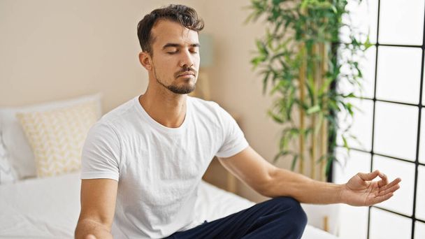 Young hispanic man doing yoga exercise sitting on bed at bedroom - Foto, Bild
