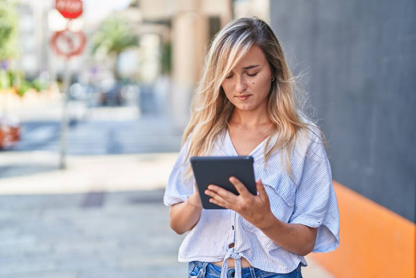 Junge blonde Frau benutzt Touchpad mit ernstem Gesichtsausdruck auf der Straße - Foto, Bild