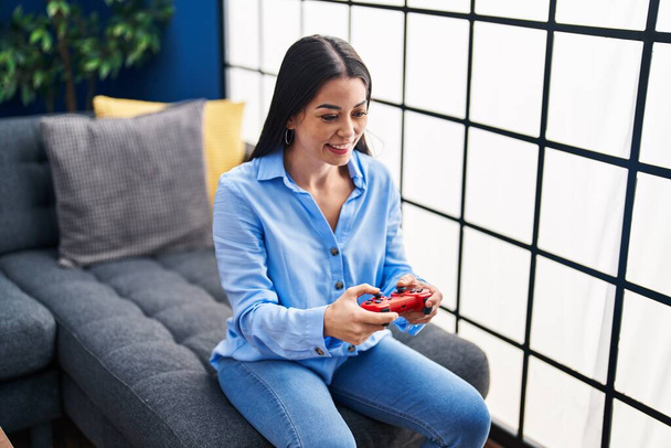 若いです美しいですヒスパニック系の女性再生ビデオゲーム座っているソファに家 - 写真・画像