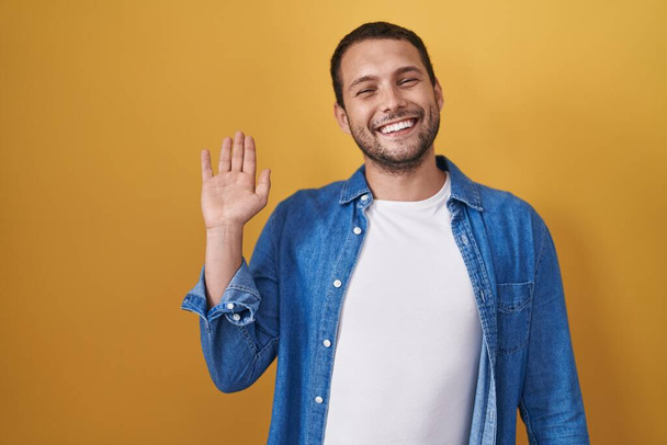 Hispánec stojí nad žlutým pozadím a vzdává se pozdravu šťastný a usměvavý, přátelské uvítací gesto  - Fotografie, Obrázek