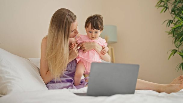 Mother and daughter using laptop sitting on bed at bedroom - Foto, afbeelding