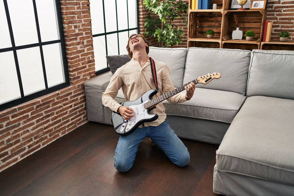 Молодий білий чоловік грає на електричній гітарі на підлозі вдома - Фото, зображення