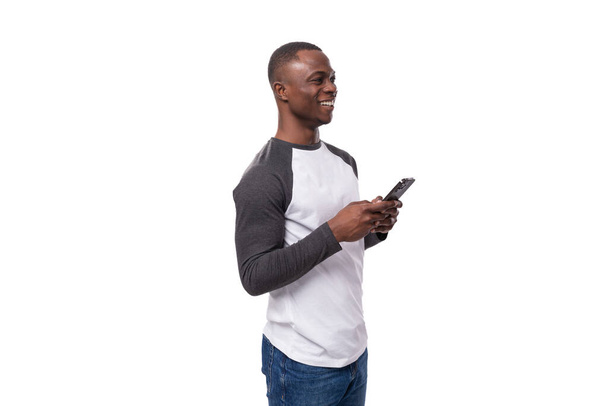 mladý ležérní americký muž s krátkým účesem oblečený v černobílém svetru a džínách držící mobilní telefon. - Fotografie, Obrázek